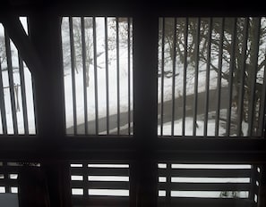 A window with vertical bars, a view of a snowy landscape with trees, and a road.