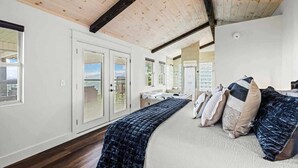 A bedroom with a large bed, wooden ceiling beams, and a view of the outdoors.