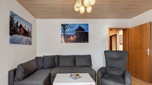 A living room with a grey sofa, a white coffee table, and a grey armchair. There are two framed pictures on the wall.