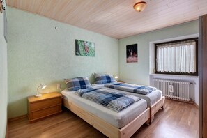 A bedroom with two beds, a nightstand, a window with curtains, and a radiator.