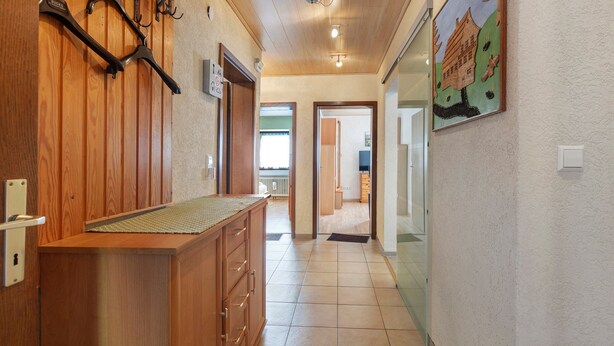 A hallway with wooden paneling, a coat rack, a painting, and a tiled floor.