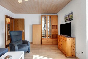 A living room with a wooden cabinet, a television, and a blue armchair.