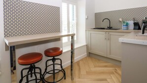 A modern kitchen with a herringbone-patterned backsplash, a wooden countertop, two stools, and a window with blinds. - Cae Gwyn (Ty Croes)
