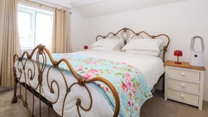 A bedroom with a bed, a nightstand, a lamp, and a window with curtains. - Cae Gwyn (Ty Croes)