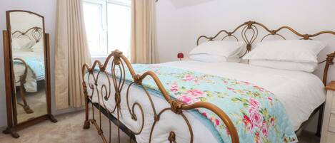 A bedroom with a bed, a mirror, a window with curtains, and a bedside table.