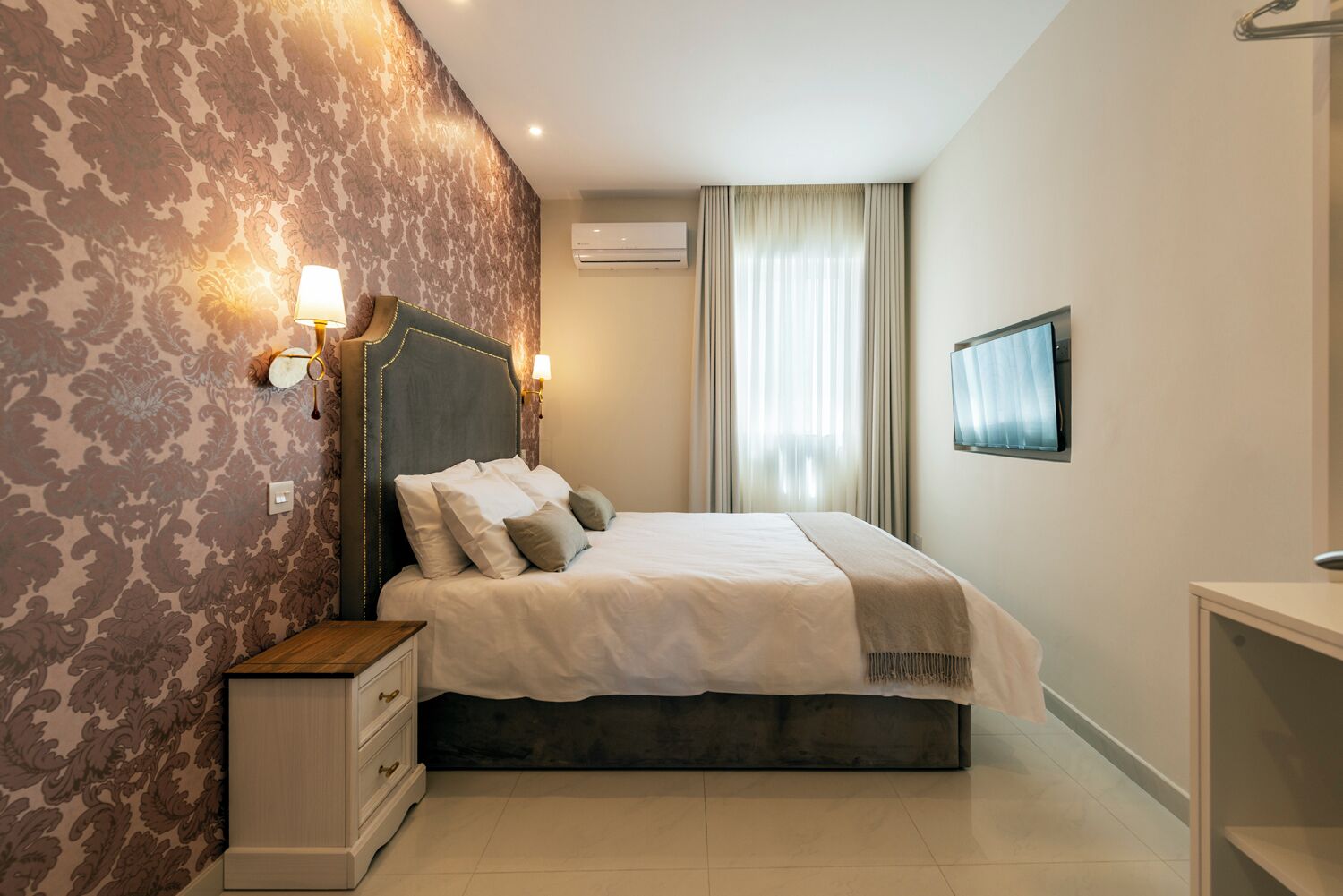 Een keurig opgemaakt slaapkamer met een bed, nachtlampjes, een televisie en een kledingkast.