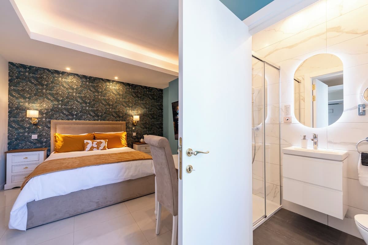 A bedroom with a bed, nightstands, and a bathroom with a shower, sink, and mirror.