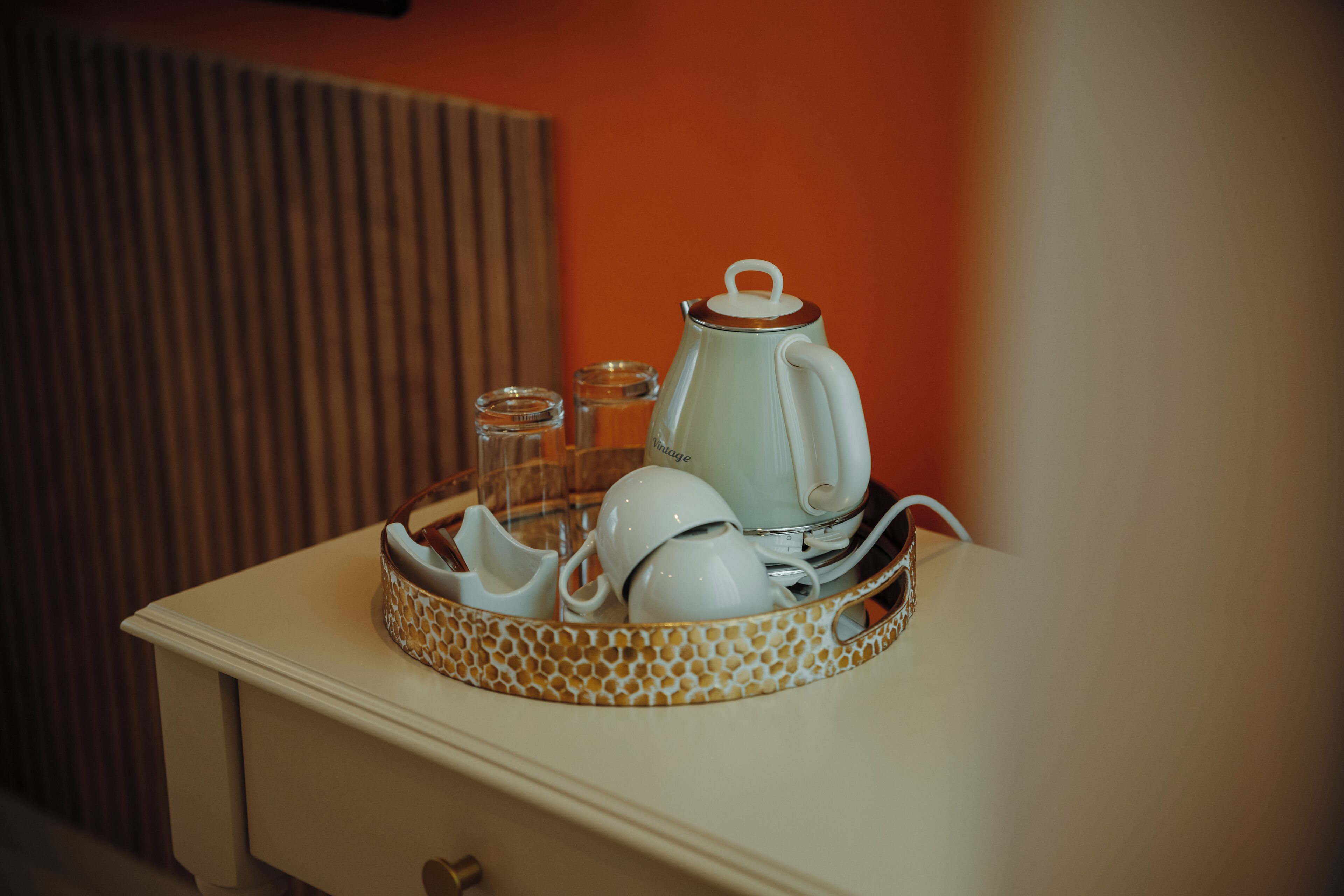 A tray with a teapot, cups, and glasses on a bedside table.