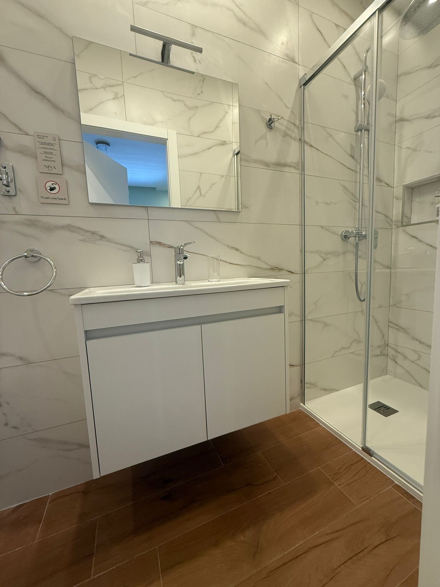 Une salle de bain moderne avec une douche en verre, un mur recouvert de carreaux de marbre et un plancher en bois.
