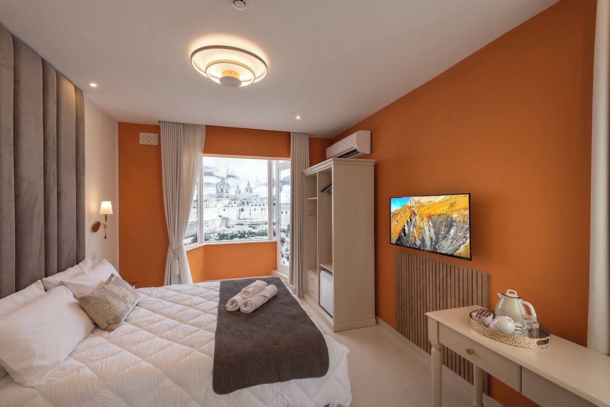 A hotel room with a bed, a view of a cityscape, a television, and a radiator.