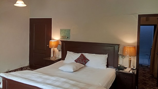 Hotelkamer met een groot bed, twee bedlampen, een houten hoofdeinde, een nachtkastje met een telefoon en een deur naar een andere kamer.