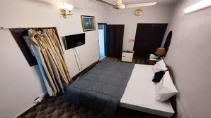Een kleine, schone kamer met een bed, een bureau, een stoel, een televisie en een raam met gordijnen.