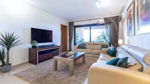 Una sala de estar moderna con un televisor de pantalla plana, un sofá, una mesa de centro y un amplio ventanal con cortinas.