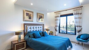 Un dormitorio moderno con una cama grande, mesitas de noche, una silla y un ventanal con cortinas.