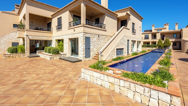 Un edificio moderno de varios pisos con piscina, muros de piedra y balcones.