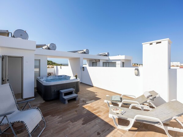 Una terraza en la azotea con jacuzzi, sillones de descanso y una cubierta de madera.