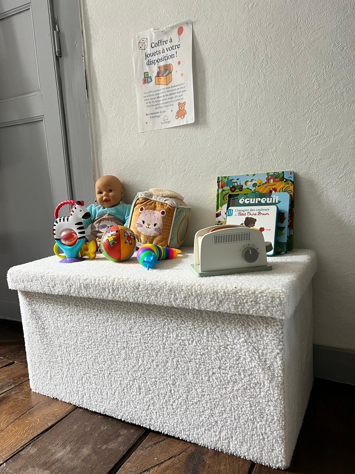 A white cushioned bench with toys and a radio, a wall with a sign, and a door.