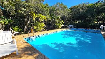 Une piscine rectangulaire dont le bord est recouvert de carrelage, entourée d’une terrasse en bois. On y trouve des chaises longues blanches et une petite table près de la piscine.