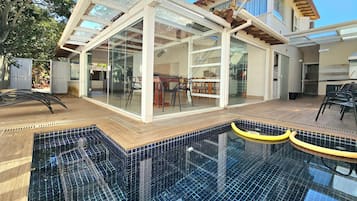 Une maison moderne dotée d’un patio entièrement vitré, d’une piscine et de mobilier d’extérieur.