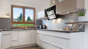 A modern kitchen with white cabinets, a built-in oven, a window with a view of trees, and a plant on the countertop.