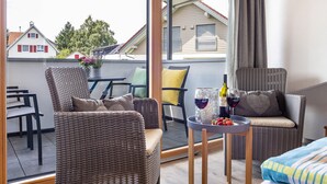 Un balcon agrémenté de meubles en osier, une table avec une bouteille de vin et des fraises, et une vue sur les maisons.