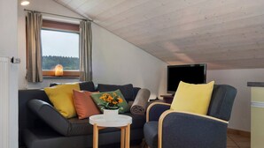A cozy living room with a sofa, armchair, TV, and a window with curtains.