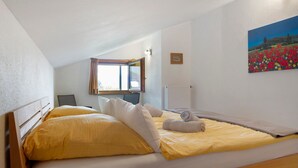 A single bed with yellow and white bedding, a window with a view of a field, and a painting on the wall.