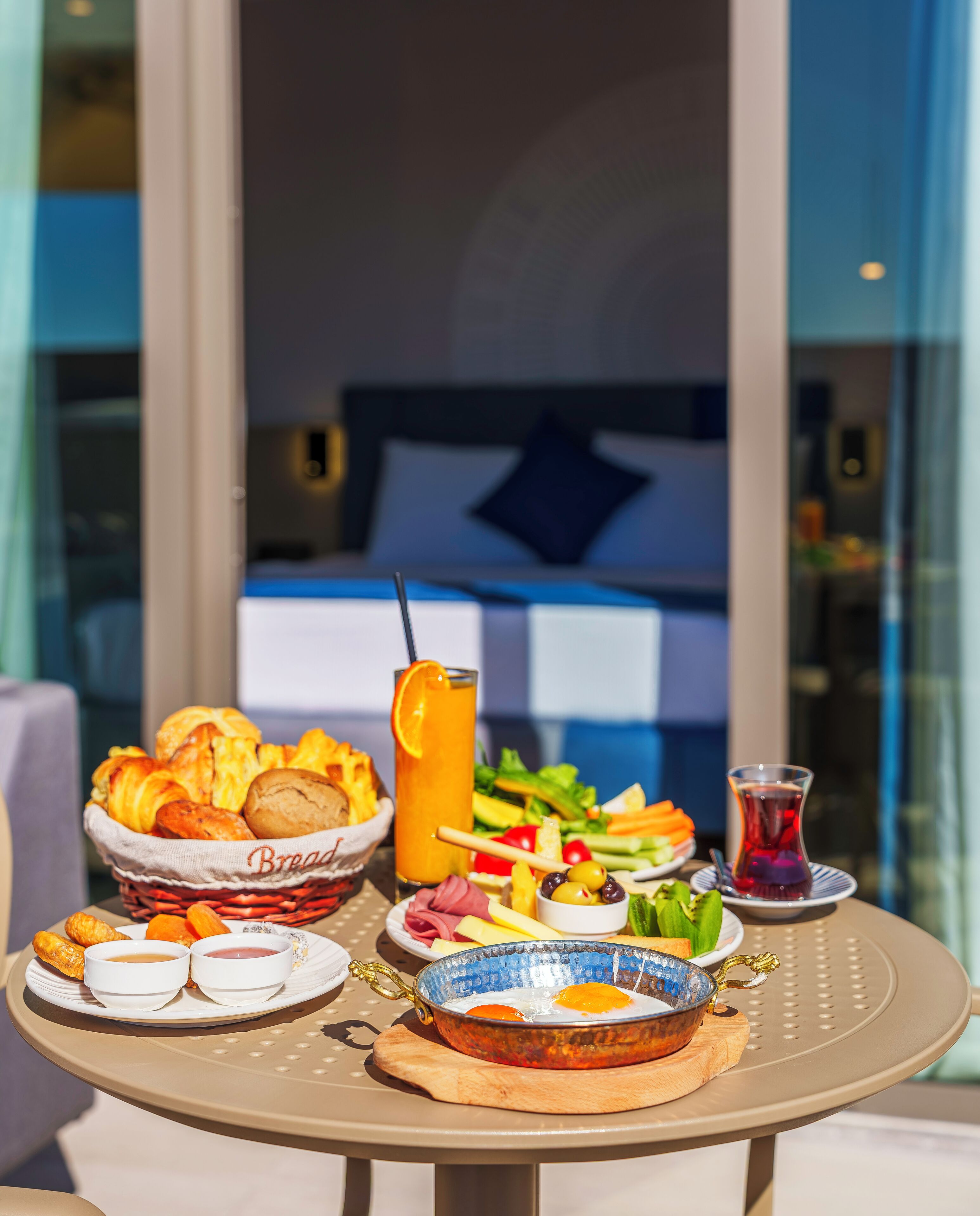 A table with a variety of breakfast items including bread, eggs, and a drink, set on a balcony with a view of a building.