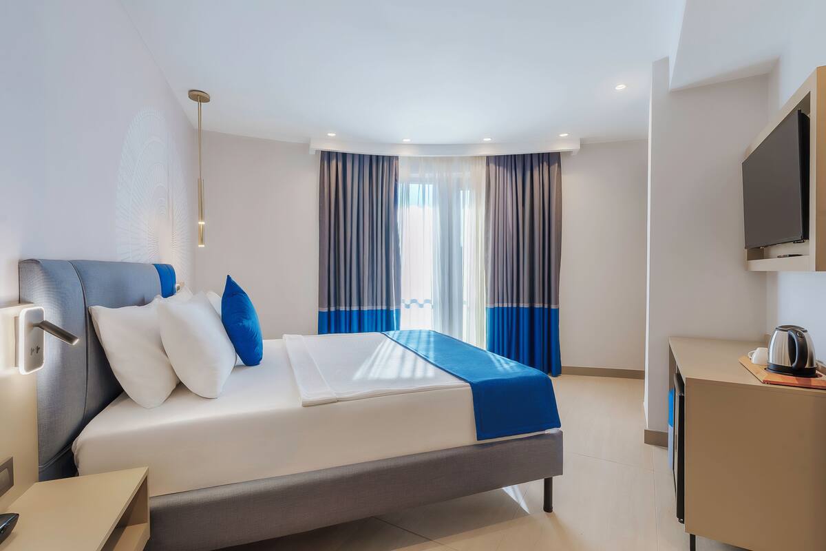 A modern hotel room with a bed, a desk, a television, and a window with curtains.
