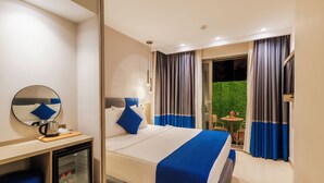 Hotelkamer met een bed, bureau met koffiezetapparaat, minibar en uitzicht op een tuin door het raam.