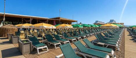 A beachside lounge area with rows of sunbeds and umbrellas, a wooden deck, and a clear sky.