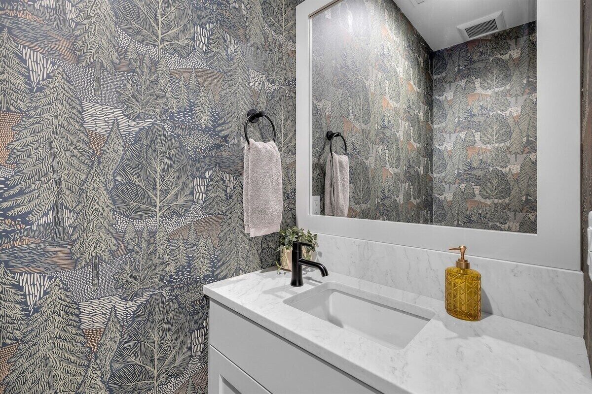 Une salle de bain avec un grand miroir, un lavabo doté d’un distributeur de savon doré et une serviette suspendue à un porte-serviettes noir.
