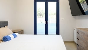Une chambre à coucher comprenant un lit, une commode en bois, une table de chevet et un téléviseur fixé au mur.