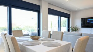 Un coin repas avec une table dressée pour quatre personnes, de grandes fenêtres et un canapé à l’arrière-plan.