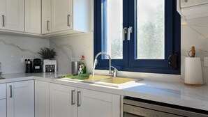 Une cuisine moderne avec des meubles blancs, un plan de travail en marbre, un évier avec un robinet, une machine à café, une plante et une fenêtre avec des volets bleus.
