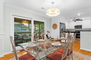 A modern kitchen with white cabinets, stainless steel appliances, and a dining area with a glass table and wicker chairs.