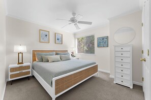 A bedroom with a bed, bedside tables, a dresser, a ceiling fan, and artwork on the walls.