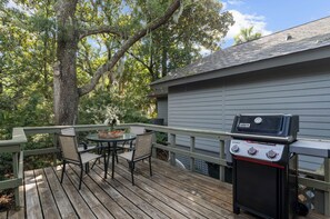 An outdoor deck with a grill, a table with chairs, and a view of a house.