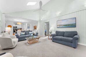 A spacious living room with a high ceiling, a large window, and a ceiling fan.