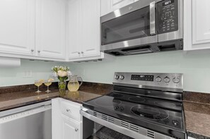 A modern kitchen with white cabinetry, a stainless steel microwave, and a black stove. - Yards to the beach, charming cottage (Kiawah Island)
