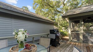 Une terrasse extérieure avec une table en verre, un panier en osier et un barbecue.