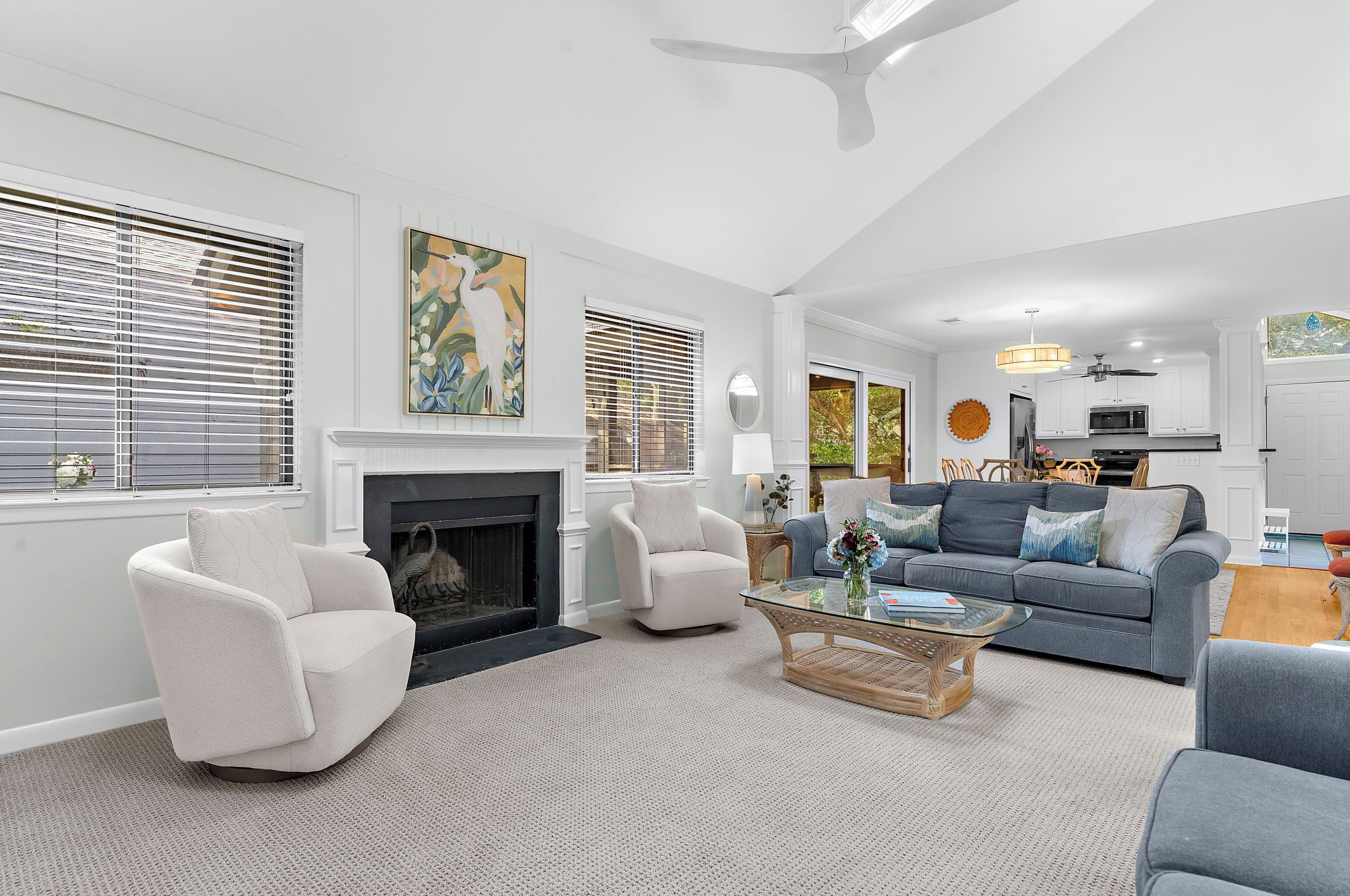 A spacious living room with a fireplace, comfortable seating, and a view of the kitchen.