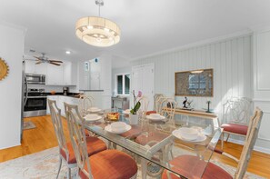 A modern kitchen with white cabinetry, stainless steel appliances, and a dining area with a glass table and wooden chairs. - Yards to the beach, charming cottage (Kiawah Island)