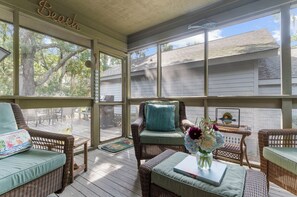 A covered porch with wicker furniture, a view of the house, and a sign that says 'Beach Life is Best.'