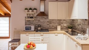 A kitchen with white cabinets, a microwave, a stove, and a sink. There are potted plants on a shelf and a bowl of fruit on the table. - T-Rooftop (Como)