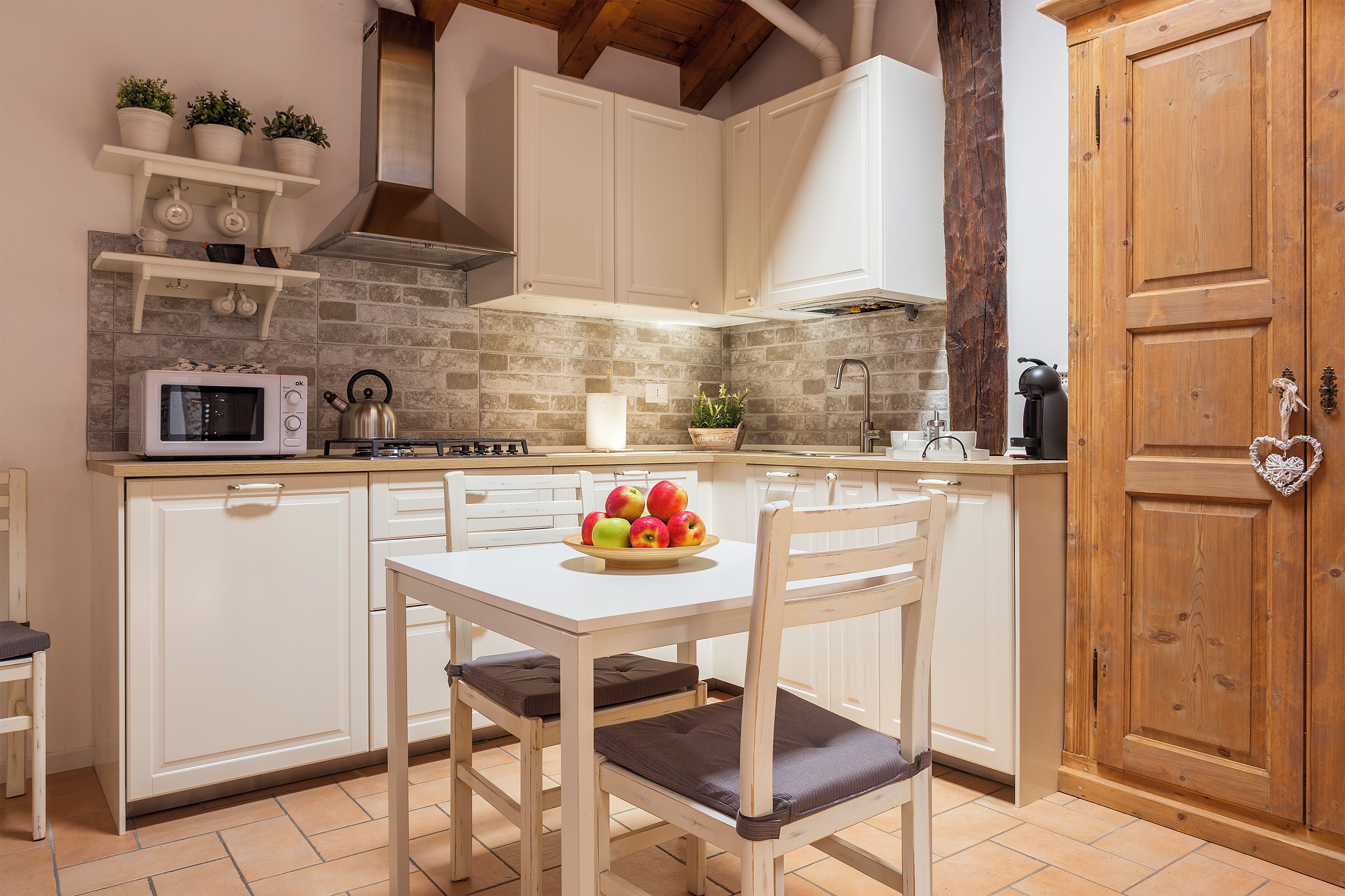 Una cocina con armarios blancos, microondas, estufa y puerta de madera.