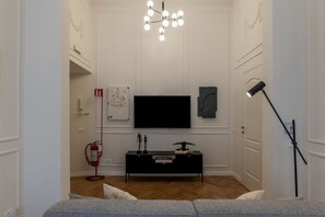 A modern living room with a flat-screen TV, a black console table, a unique chandelier, and a floor lamp.