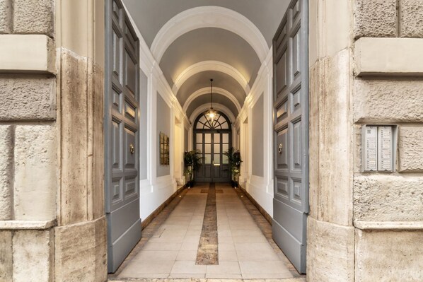 A hallway with arched ceilings and double doors, leading to a room with a large window and a door.