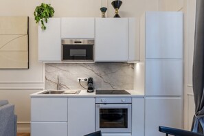 A compact kitchen with white cabinetry, a built-in oven, a microwave, and a coffee maker.