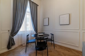 A dining area with a round table, four chairs, and two framed artworks on the wall.